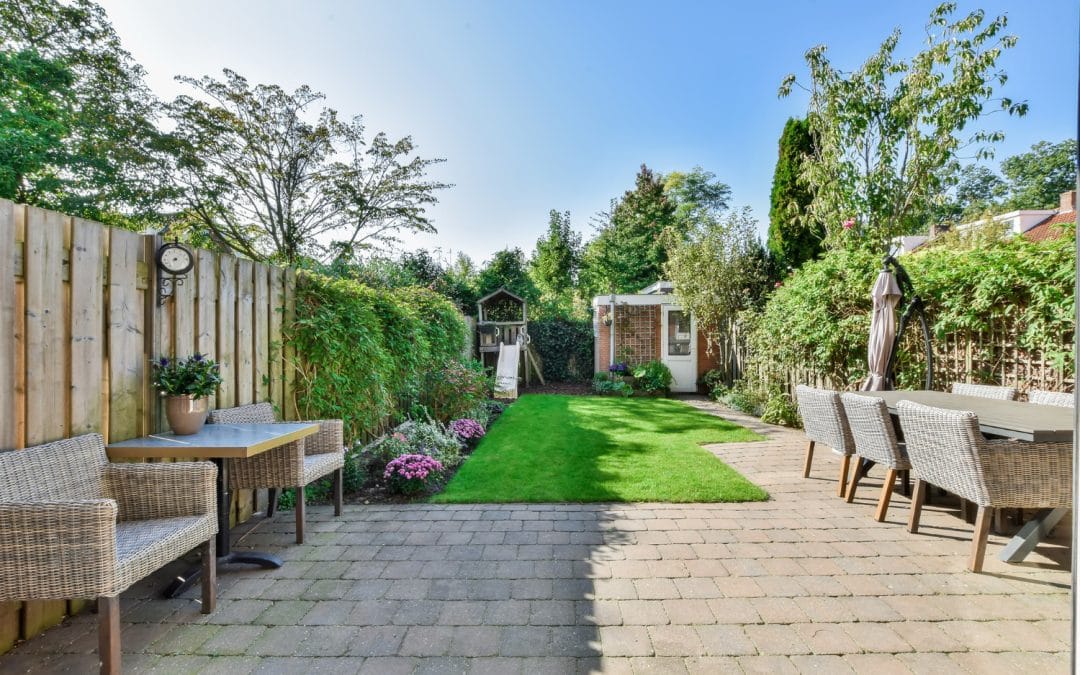 Neat backyard with patio furniture, potted plants, green lawn, and a small garden shed at the back.